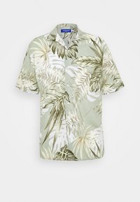 Lyhythihainen nappikauluspaita, jossa on vihreä ja beige trooppinen lehtikuvio vaaleanvihreällä taustalla.