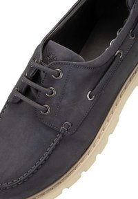 Marineblaue Lederbootsschuh mit beiger Gummisohle, vier Ösen für Schnürsenkel und sichtbarem Nähdetail entlang der Kante.