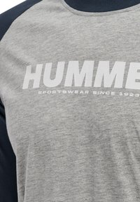 Grå sportswear-shirt med navy ærmer med teksten "HUMME" og "SPORTSWEAR SINCE 1923" trykt i hvidt på brystet.