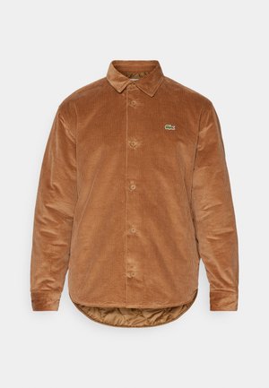 Brown corduroy shirt with a classic collar, button closure, long sleeves, and a small green Lacoste logo on the left chest. Textured surface.