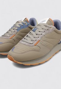 Baskets beiges avec une tige en matériaux mixtes, présentant des accents en suède gris, des détails bleus, des touches oranges et une semelle gris clair.