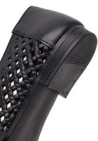 Tacco di scarpa in pelle nera con pannello laterale intrecciato e suola in gomma testurizzata e zigrinata per grip e durata.