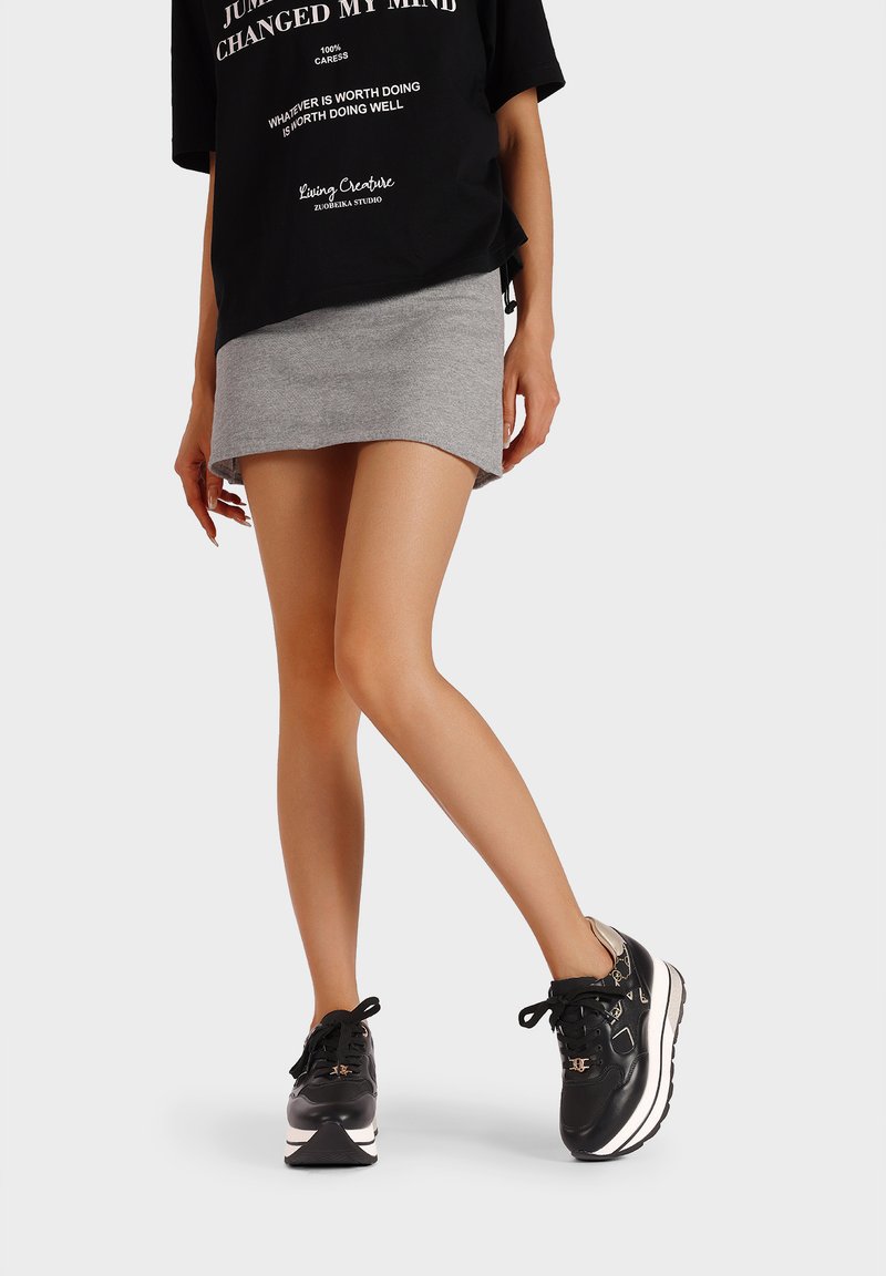 Maglietta grafica nera, gonna mini grigia e sneakers nere con suola bianca. L'outfit presenta una vestibilità rilassata e uno stile casual.