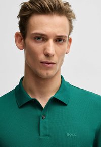 Polo verde realizzato in tessuto strutturato, con patta a tre bottoni e discreto logo "BOSS" ricamato sul petto.