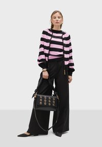 Felpa con cappuccio a strisce nere e rosa, zip frontale, abbinata a pantaloni neri a gamba larga. Presenta una borsa nera con borchie dorate quadrate.