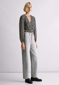 Bijela i crna košulja dugih rukava s dubokim V-izrezom, uparen s visokim svijetlosivim trapericama ravnog kroja i crnim mokasinkama.