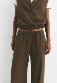 Gilet corto a righe bianche e marroni con orlo elasticizzato abbinato a pantaloni larghi con vita regolabile mediante cordino.