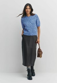 Blue textured knit sweater with short sleeves, paired with a long black leather skirt. Footwear is black lace-up boots, holding a brown handbag.