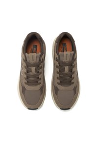 Zapatillas deportivas marrones con acentos de malla, punta redondeada, diseño con cordones y suela contrastante. Texturas notables incluyen patrones lisos y perforados.