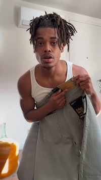 Άνδρας με λευκό αμάνικο πουκάμισο κρατά γκρι τζιν με ετικέτες σε φωτεινό δωμάτιο, δείχνοντας σε ετικέτα κοντά στη μέση.