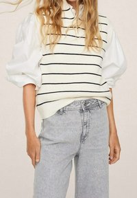 Knit sleeveless sweater in cream with navy stripes, paired with light grey high-waisted jeans. Features a relaxed fit and textured fabric.