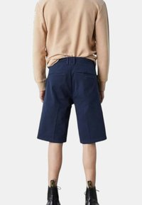 Shorts di cotone blu navy con taglio dritto, alla lunghezza del ginocchio, dotati di due tasche posteriori e una texture liscia, abbinati a un maglione beige.