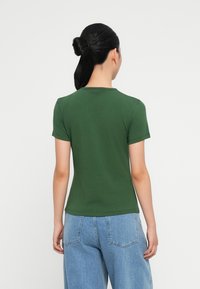 Camiseta de algodón verde con mangas cortas, cuello redondo y corte ajustado. Lleva puesta unos vaqueros de denim de talle alto en azul claro.