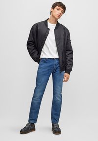 Chaqueta bomber negra, camiseta blanca, jeans azules y zapatillas negras. La bomber cuenta con puños acanalados y un acabado suave.