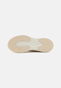 Såle av en sneakers, med et teksturert gummidesign i beige og hvit, samt et detaljert mønster for grep og støtte.