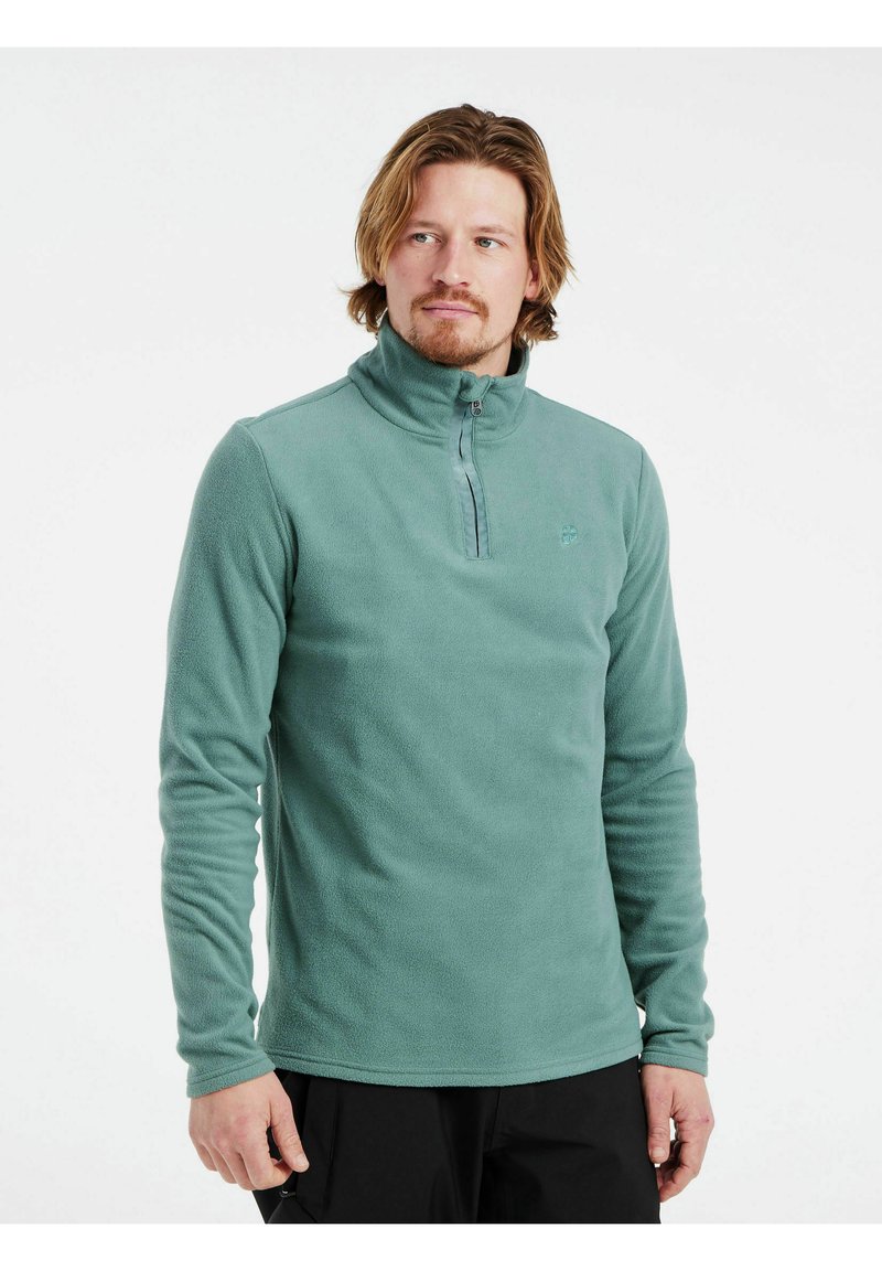 Grön fleecepullover med hög krage, utrustad med dragkedja framtill och långa ärmar. Slät textur och subtil logotypdetalj på bröstet.