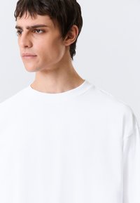 Hvit T-skjorte med korte ermer, rund hals, glatt tekstur og avslappet passform, med diskrete sømmer langs kantene.