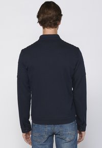 Hanorac bleumarin cu guler înalt, țesătură texturată, manșete cu nervuri și detalii accent pe umeri. Asortat cu blugi din denim.