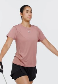 Kortärmad, ljusrosa sportt-shirt med rund halsringning och en liten vit logotyp på bröstet, i kombination med svarta löparshorts.