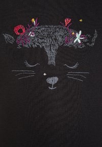 Černá látka s propracovaným šedým vyšíváním kočičího obličeje a květinovými akcenty v růžové, fialové, žluté a bílé barvě.
