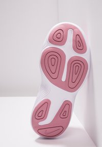 Bílá a růžová podrážka sportovní obuvi s texturovaným gripem a logem Nike, umístěná svisle proti bílé rohu stěny a podlahy.