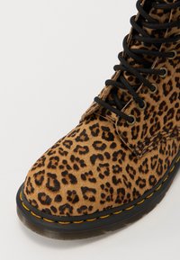 Ankle botine s uzorkom leoparda izrađene od mekog, teksturiranog materijala s crnim vezicama, žutim šavovima i debelim crnim gumenim potplatom.