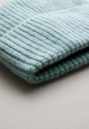 Bonnet tricoté bleu clair avec une texture côtelée, fabriqué en laine douce. Replié soigneusement pour mettre en valeur le design et la qualité du matériau.