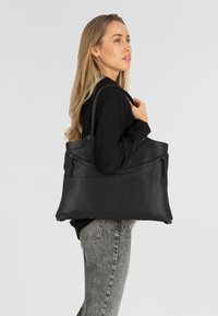 Sac tote en cuir noir avec une finition texturée, des poignées supérieures doubles et une poche zippée à l'avant. Design simple et moderne.