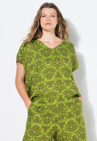 Top verde con motivo a fantasia, con scollo a V e maniche corte, realizzato in tessuto leggero. Presenta intricati motivi floreali di colore verde scuro.