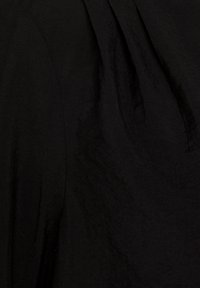 Tessuto nero con una superficie morbida e testurizzata, caratterizzato da sottili pieghe e dettagli drappeggiati, probabilmente parte di un design per un indumento.