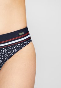 Námořnické bikiny s květinovým bílým vzorem, červenými a světle modrými pruhy v pase, hladká textura a malá metalická visačka.