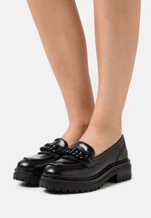 Mocassins en cuir noir avec une semelle épaisse et un détail en chaîne sur le devant. Texture lisse avec un design épuré et un bout arrondi.
