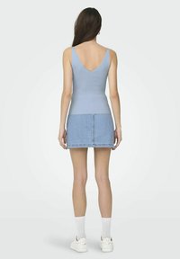 Lichtblauw geribbeld tanktop met een diepe V-rug, gecombineerd met een denim minirok. Witte enkelsokken en sneakers maken de look compleet.