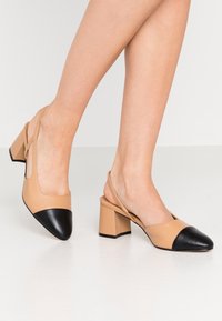 Beige slingback shoes with a black pointed toe and block heel, featuring smooth leather material and a minimalistic design.