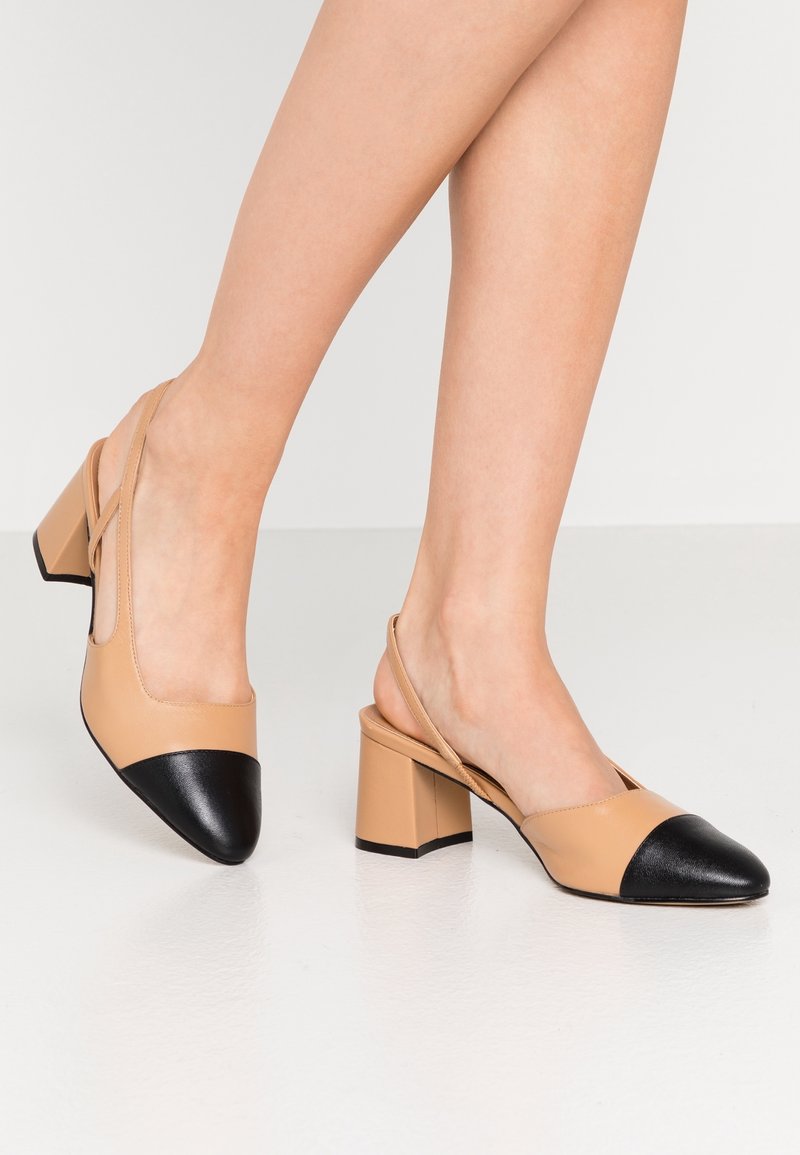 Beige slingback shoes with a black pointed toe and block heel, featuring smooth leather material and a minimalistic design.