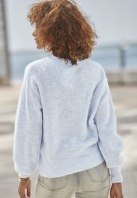 Hellblauer, flauschiger Strickpullover mit lockerer Passform, gerippter Struktur und langen Ärmeln. Kombiniert mit hellen Jeans.