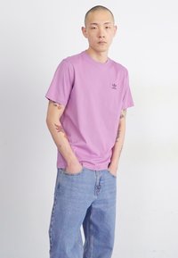 Rózsaszín pamut póló rövid ujjakkal és kerek nyakkivágással. Egy kis fekete Adidas logó található a mellkasi részen, mellé pedig laza kék farmernadrág.