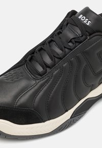 Baskets en cuir noir avec lacets noirs, logo "BOSS" sur la languette, et semelle en caoutchouc texturé blanc et noir.