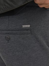 Mörkgrå byxor i ett texturerat tyg, med en framficka som har en silverfärgad "JACK & JONES"-tagg och en svart knappdetalj.