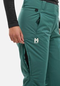Türkise Skihosen aus synthetischem Material, mit einer Reißverschlussbelüftungstasche, verstellbarem Bund und einem Markenlogo auf dem Oberschenkel.