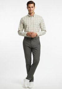 Camisa de cuadros abotonada en tonos crema y verde, combinada con pantalones ajustados grises y zapatillas blancas; tela suave con detalles de textura sutil.