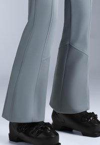 Grå skidbyxor med utsvängd design och strukturerad tyg, i kombination med svarta skidstövlar med justerbara spännen och en slät finish.