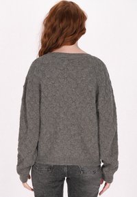 Szürke kötött pulóver laza szabással, gyémántmintával és bordás mandzsettával, sötétszürke farmerral párosítva.