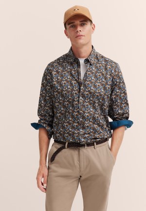 Brown floral-patterned button-up shirt with blue accents, paired with beige pants and a brown braided belt. Casual cap completes the look.
