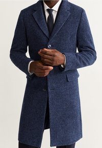 Cappotto di lana blu navy con vestibilità sartoriale, chiusura a un bottone, rever a scollo a V e due tasche frontali. Tessuto strutturato con un motivo sottile.
