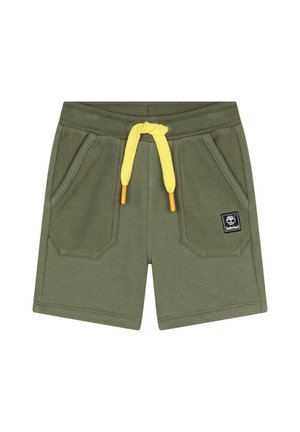 Pantaloni corti verde oliva in un materiale morbido con una finitura testurizzata, dotati di tasche frontali e di un laccetto giallo brillante. Incluso un piccolo patch con logo.