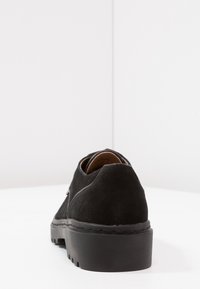 Scarpa in suede nera con tacco basso e suola testurizzata. Presenta un retro arrotondato e cuciture minime lungo le giunture.