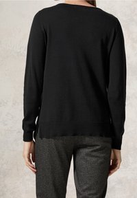 Svart tröja med lös passform, rund halsringning och ribbad nederkant. Texturerade grå houndstooth-byxor delvis synliga nedtill.