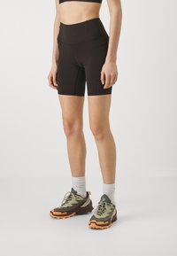Schwarze, hoch taillierte Shorts mit einem eleganten Design. Sie verfügen über einen glatten Stoff und eine figurschmeichelnde Silhouette. Kombiniert mit olivgrünen und orangenen Sportschuhen.