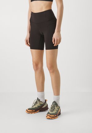 Pantaloni corti neri a vita alta con un design elegante. Presentano un tessuto morbido e una silhouette aderente. Indossati con scarpe da ginnastica color oliva e arancione.